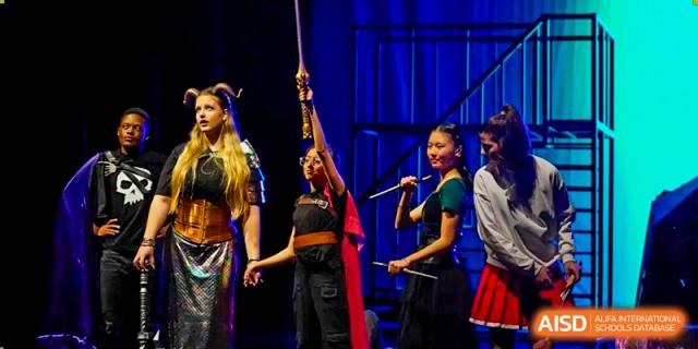 Three female students perform on stage with props and flags during a school production or cultural event at Shanghai Community International School.