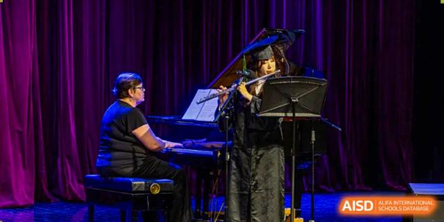 A student in a black outfit plays the flute while another plays the keyboard during a musical concert at Shanghai Community International School.
