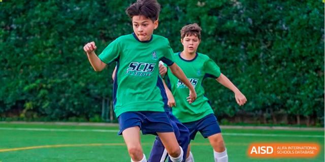 Two students wearing green athletic uniforms with the SCIS logo run across a field during a sports practice or game at Shanghai Community International School.