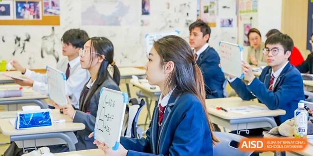 A female student in a uniform holds a small whiteboard with chemical structures, participating in a class discussion at Shanghai DTD Academy.