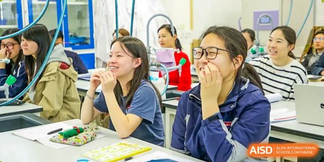 Two female students smile and engage in a class discussion or group project around a table at Shanghai DTD Academy.
