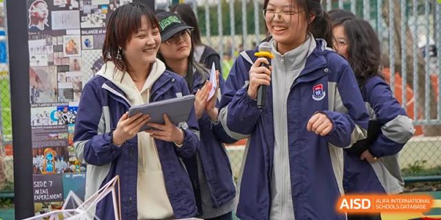 Students stand and collaborate on a project, with one holding a digital tablet, during an interactive class at Shanghai DTD Academy.