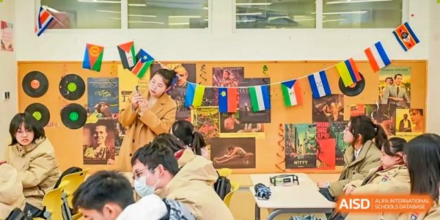 Students gather in a common area decorated with international flags and posters, engaged in a casual discussion or social event at Shanghai DTD Academy.