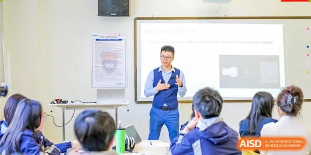 A male teacher in a blue vest lectures students while pointing to a screen or whiteboard during a classroom session at Shanghai DTD Academy.