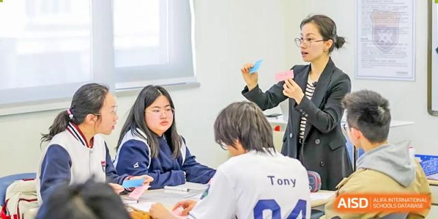 Two students sit at a table collaborating on an assignment while a teacher offers guidance in a classroom at Shanghai DTD Academy.