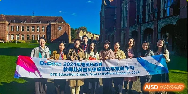 A group of teachers and staff members from Shanghai DTD Academy stand outdoors holding a banner in front of a traditional-style brick building during a professional development trip.