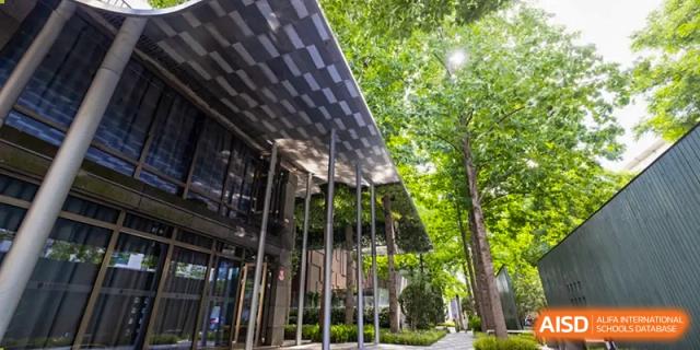 A view of the modern, glass and metal entrance or walkway of Shanghai DTD Academy, surrounded by lush green trees and landscaping.
