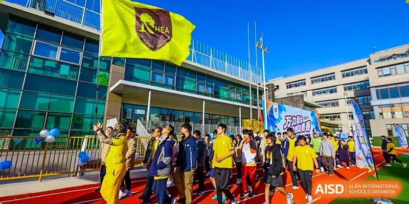 A large group of students in jackets and backpacks walk together outside an academic building on the campus of Shanghai DTD Academy.