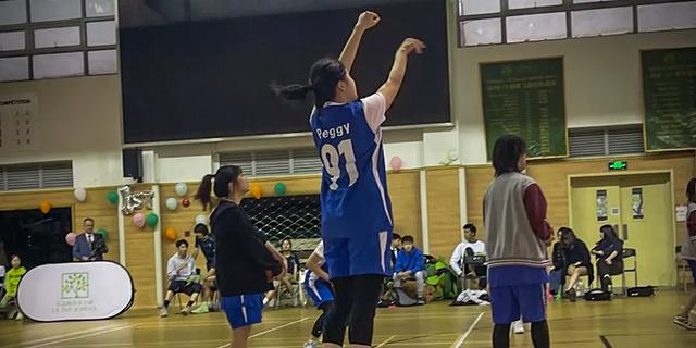 A female student athlete wearing a blue jersey shoots a basketball during an indoor game at Shanghai DTD Academy.