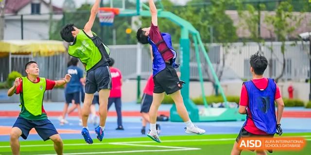 A male student athlete in a blue and red uniform jumps high to catch or shoot a ball during an outdoor sports activity at Shanghai DTD Academy.