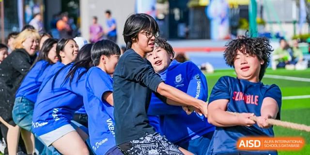 A male student warmly hugs a younger student on a sports field, showing camaraderie and support at Shanghai DTD Academy.