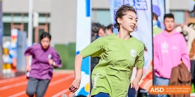 A female student in a light green t-shirt smiles brightly while participating in an outdoor activity or sport at Shanghai DTD Academy.