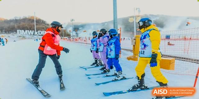 A line of students wearing helmets and brightly colored blue and purple ski gear are ready for a lesson on a snowy slope during a trip organized by Shanghai DTD Academy.