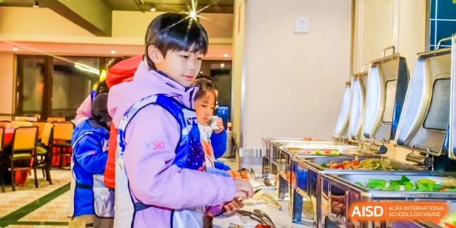 A young male student serves himself food from a buffet line during a meal or event focused on Health & Nutrition at Shanghai DTD Academy.