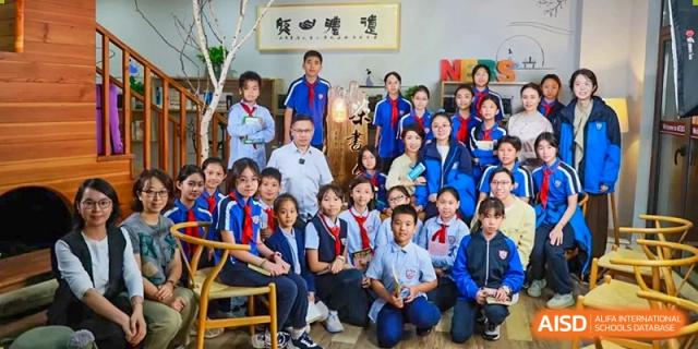 A large group of students and a teacher from Shanghai New Epoch Bilingual School smiling for a formal group photo indoors.
