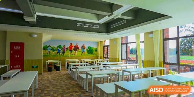 The empty dining hall or multi-purpose room at Shanghai New Epoch Bilingual School with rows of tables and colorful mural on the wall.