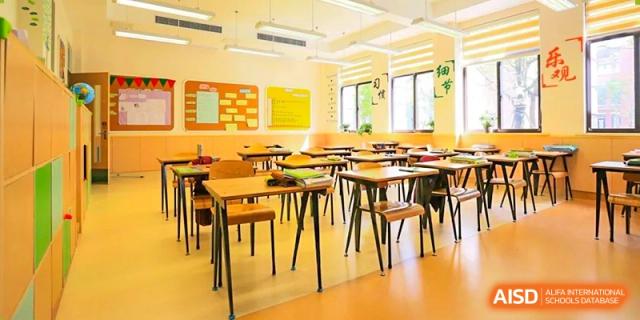 An empty, brightly lit classroom at Shanghai New Epoch Bilingual School with rows of wooden desks and chairs, and bulletin boards on the wall.