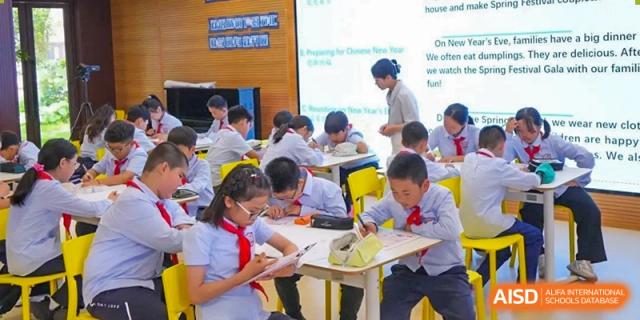 Students from Shanghai New Epoch Bilingual School working at their desks in a classroom with a teacher standing near a projection screen.