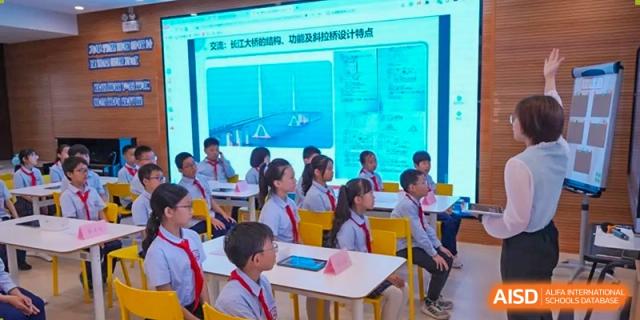Students from Shanghai New Epoch Bilingual School in uniforms sitting at desks and looking at a large screen displaying a presentation with technical diagrams or text.
