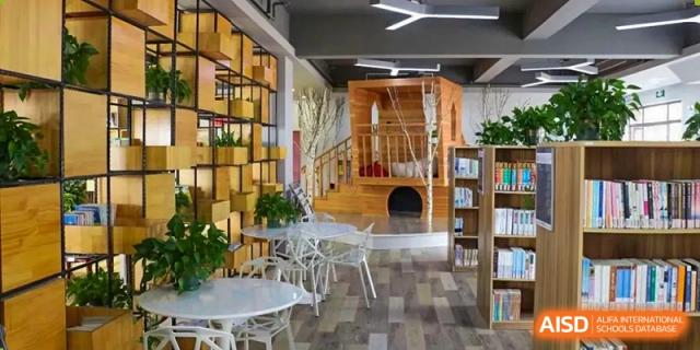 A different view of the light-filled study area at Shanghai New Epoch Bilingual School library, featuring white tables and creative architecture.