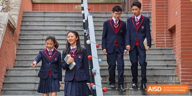 Two students from Shanghai New Epoch Bilingual School in formal school uniforms walking up or down an interior staircase.