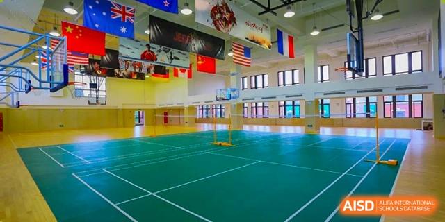Shanghai New Epoch Bilingual School indoor gymnasium with badminton and basketball courts, featuring various national flags hanging from the ceiling.