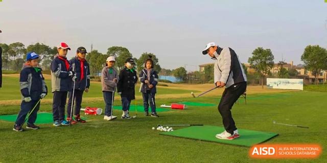 Students from Shanghai New Epoch Bilingual School receiving a golf lesson from an instructor on a green practice area.