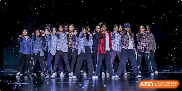 A group of students from Shanghai New Epoch Bilingual School performing a dance or standing together on a stage in casual plaid shirts and dark pants.
