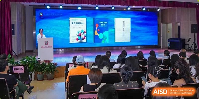An indoor presentation or lecture at Shanghai New Epoch Bilingual School with an audience of students and adults watching a screen displaying course materials or school publications.