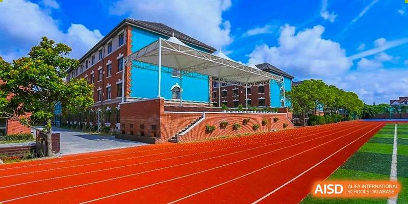 The distinctive blue and terracotta architecture of a building at Shanghai New Epoch Bilingual School next to a vibrant red running track and bleachers.