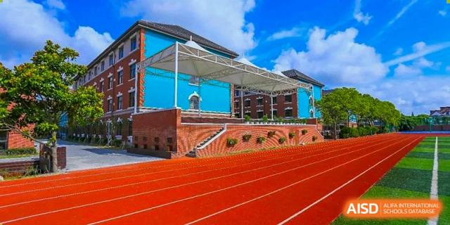 The distinctive blue and terracotta architecture of a building at Shanghai New Epoch Bilingual School next to a vibrant red running track and bleachers.