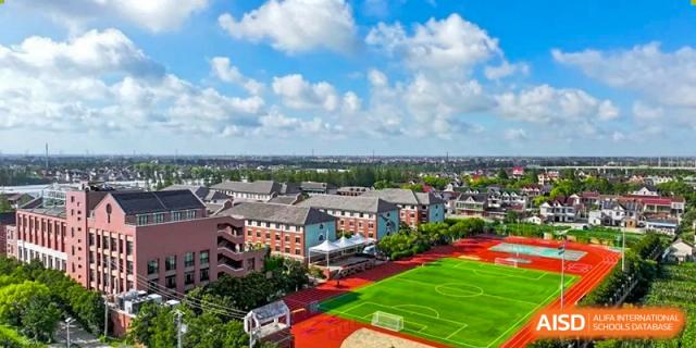 Aerial view of the Shanghai New Epoch Bilingual School campus showing school buildings and a red outdoor sports field under a blue sky.