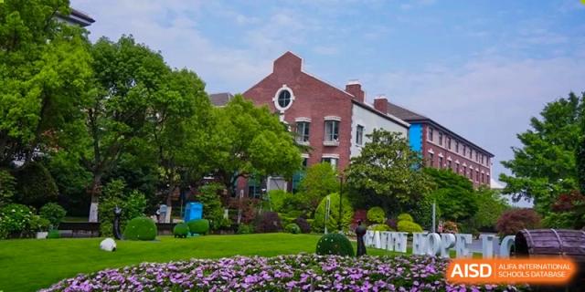 The traditional red-brick architecture of a building at Shanghai New Epoch Bilingual School, surrounded by a well-maintained green garden and purple flowers.