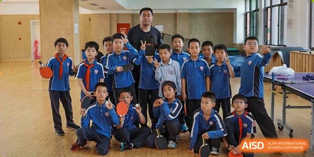 A group of young students from Shanghai New Epoch Bilingual School posing with their table tennis paddles alongside their coach.