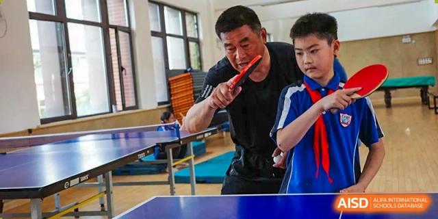 A coach at Shanghai New Epoch Bilingual School demonstrating a technique with a table tennis paddle to a student.