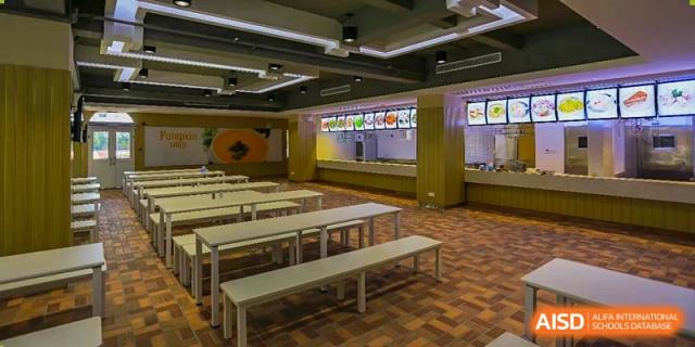 The interior of the canteen or dining hall at Shanghai New Epoch Bilingual School with rows of long wooden tables and benches.