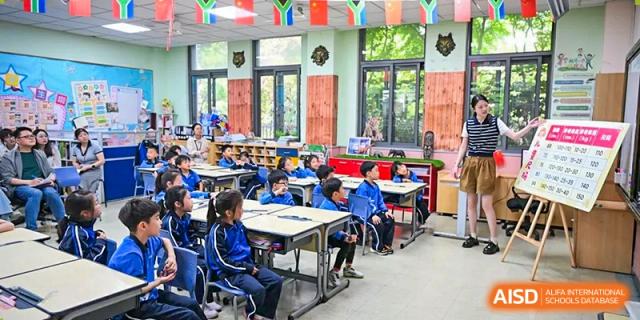 Students in uniform seated at desks and working in a brightly lit classroom with large windows overlooking trees at Shanghai United International School, Wanyuan Campus.