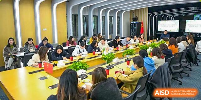 A group of students and adults seated around a long table in a meeting or seminar room, engaged in discussion at Shanghai United International School, Wanyuan Campus.