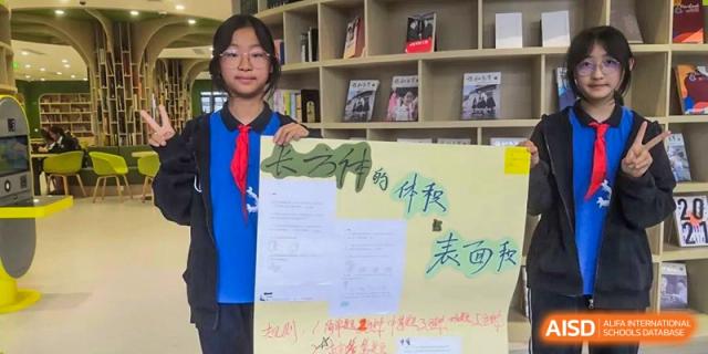 A female student holding up a presentation board with Chinese writing in front of bookshelves at Shanghai United International School, Wanyuan Campus.
