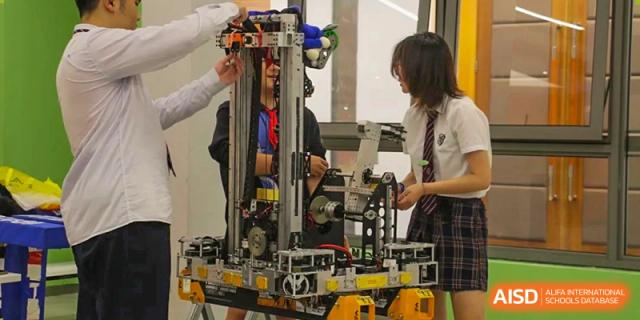 Students working on a complex piece of robotics or machinery in a workshop, focusing on the mechanical components at Shanghai United International School, Wanyuan Campus.
