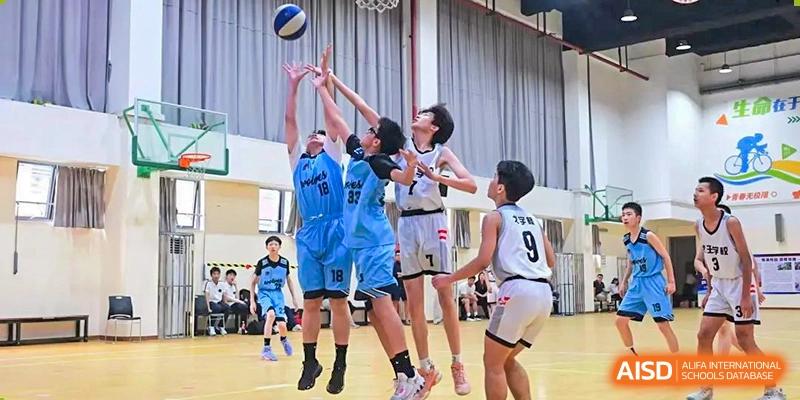 Students from opposing teams jumping for the ball during a competitive basketball game inside the gymnasium at Shanghai United International School, Wanyuan Campus.