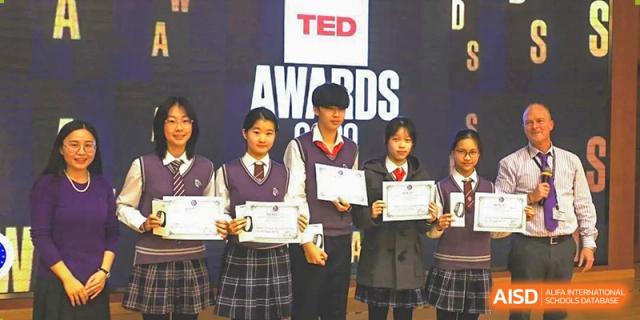 Three students in school uniform holding award certificates on stage under a large TED AWARDS banner at Shanghai United International School, Wanyuan Campus.