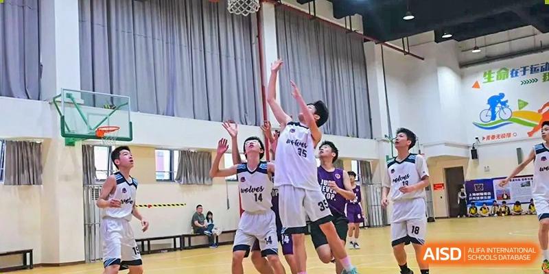 A fast-paced moment in a basketball game showing players reaching for a rebound under the hoop at Shanghai United International School, Wanyuan Campus.