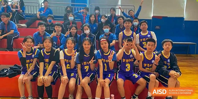 A girls' basketball team in blue and gold uniforms posing for a photo on a bench in the gymnasium at Shanghai United International School, Wanyuan Campus.