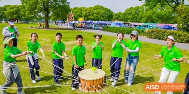Students in matching green shirts participating in a team-building or traditional drumming activity outdoors at Shanghai United International School, Wanyuan Campus.
