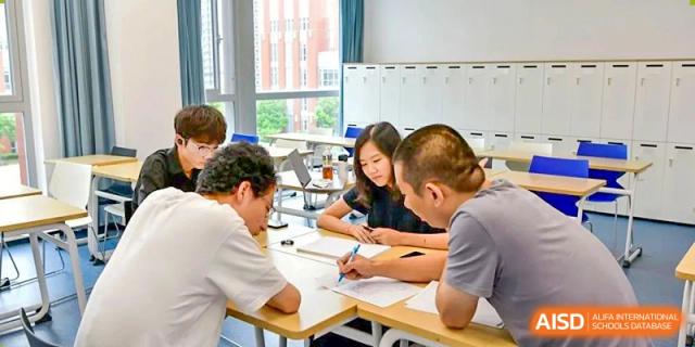 A small group of students from SHENGHUA ZIZHU ACADEMY collaborating on a task or project while seated around a table.