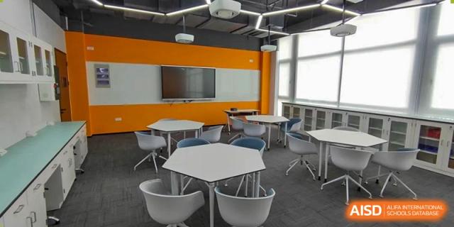 A collaborative learning space at SHENGHUA ZIZHU ACADEMY featuring unique hexagonal tables and comfortable white and blue chairs, with a large screen on the orange wall.