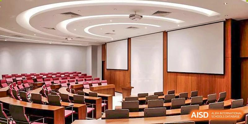 A tiered lecture hall or auditorium at SHENGHUA ZIZHU ACADEMY with brown seats, wood paneling, and a large projection screen for presentations.