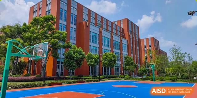 The main academic building of SHENGHUA ZIZHU ACADEMY, a multi-story, modern structure with orange and glass facades, overlooking a blue outdoor sports court.