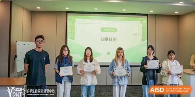 Three female students from SHENGHUA ZIZHU ACADEMY holding certificates or awards while standing in front of a presentation screen.